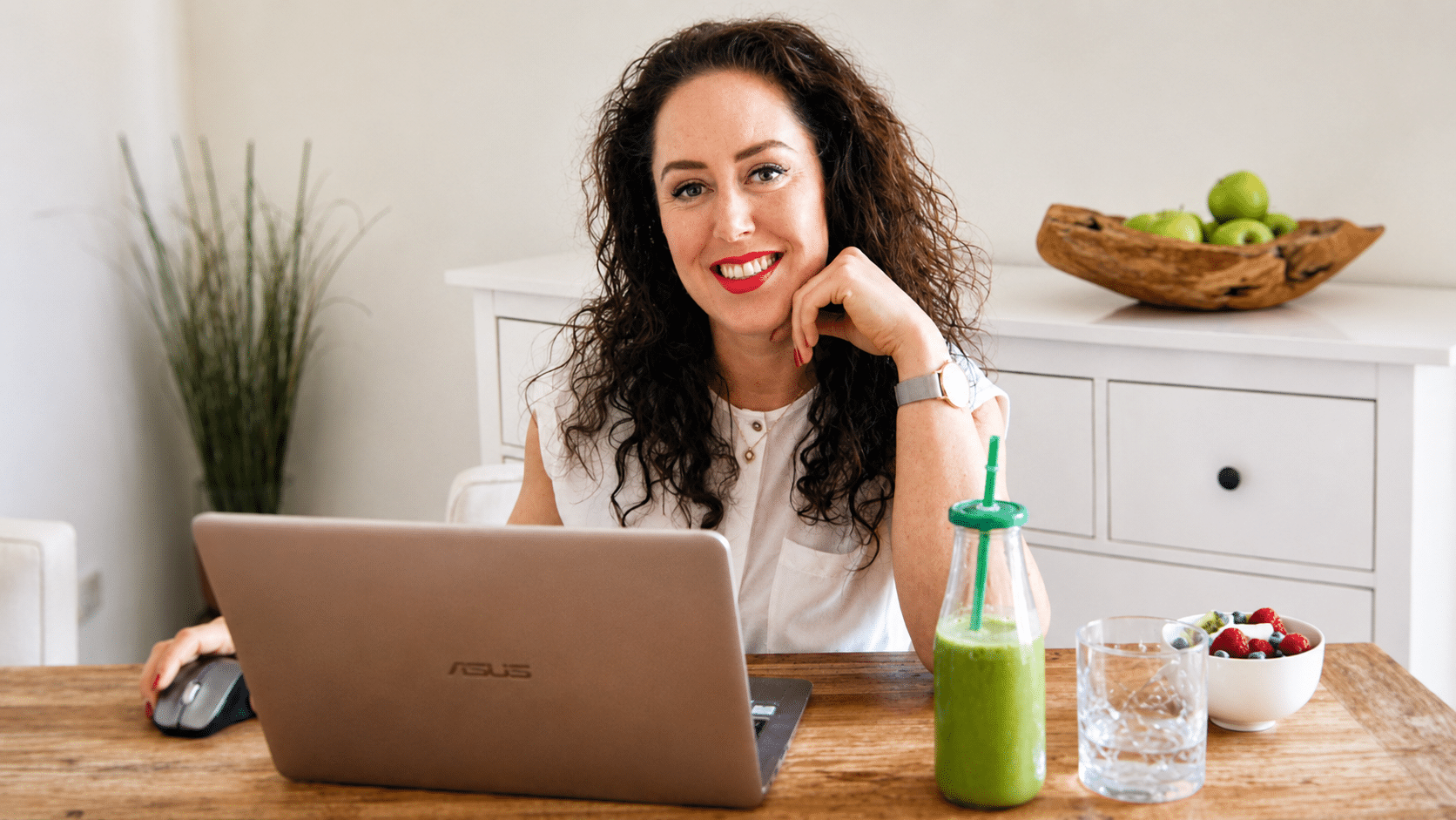 Janneke van der Linden achter haar laptop met een groene smoothie aan tafel